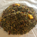 Close-up of Hammer Time herbal wellness tea blend with dried botanicals and herbs on a light fabric surface.