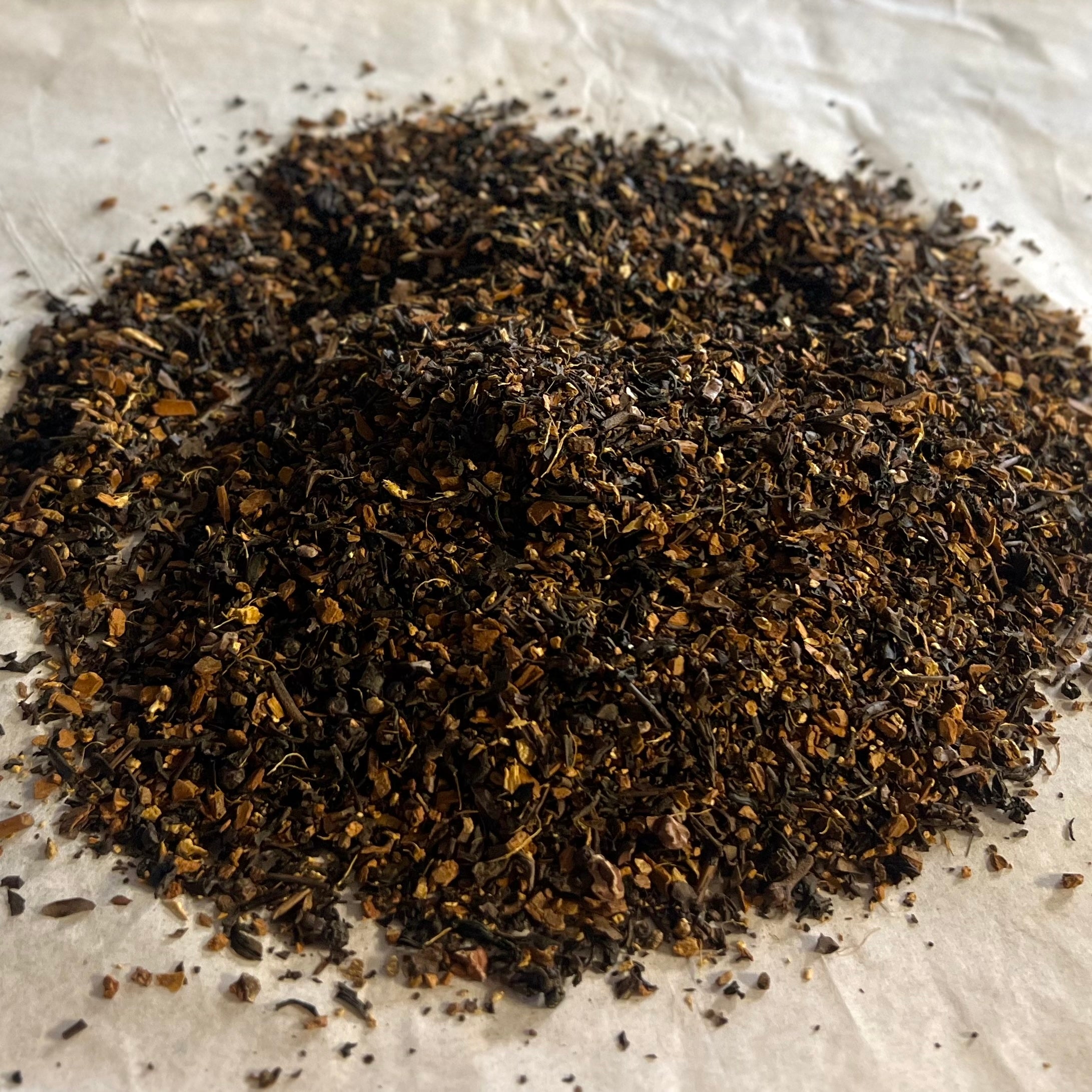 Close-up of Oh My! All the Chai Sampler loose tea blend with dark, finely chopped spicy chai ingredients on parchment paper