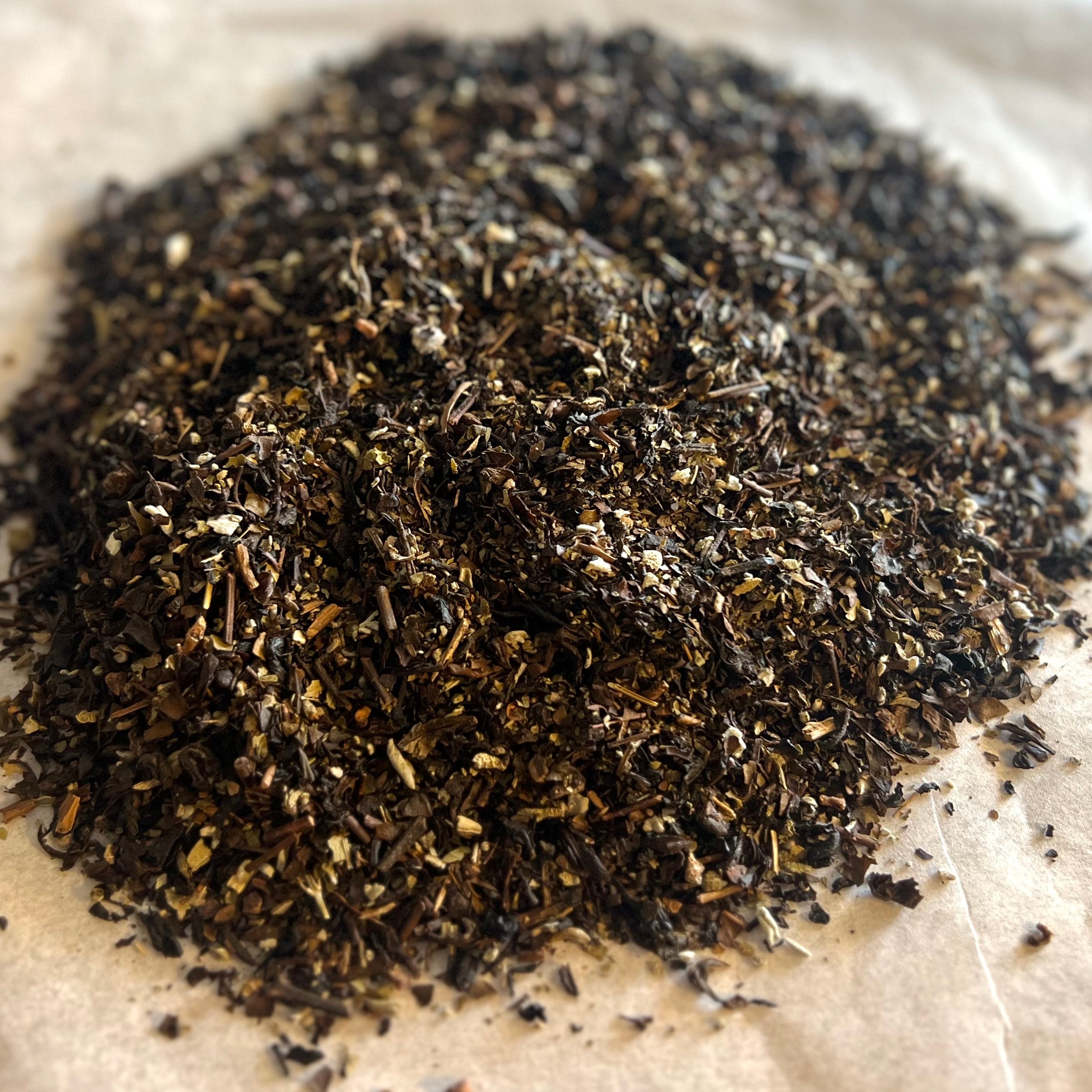 Close-up of Oolong Berry Bliss loose leaf tea blend with dark oolong leaves, dried berries, and hints of sage on parchment paper.