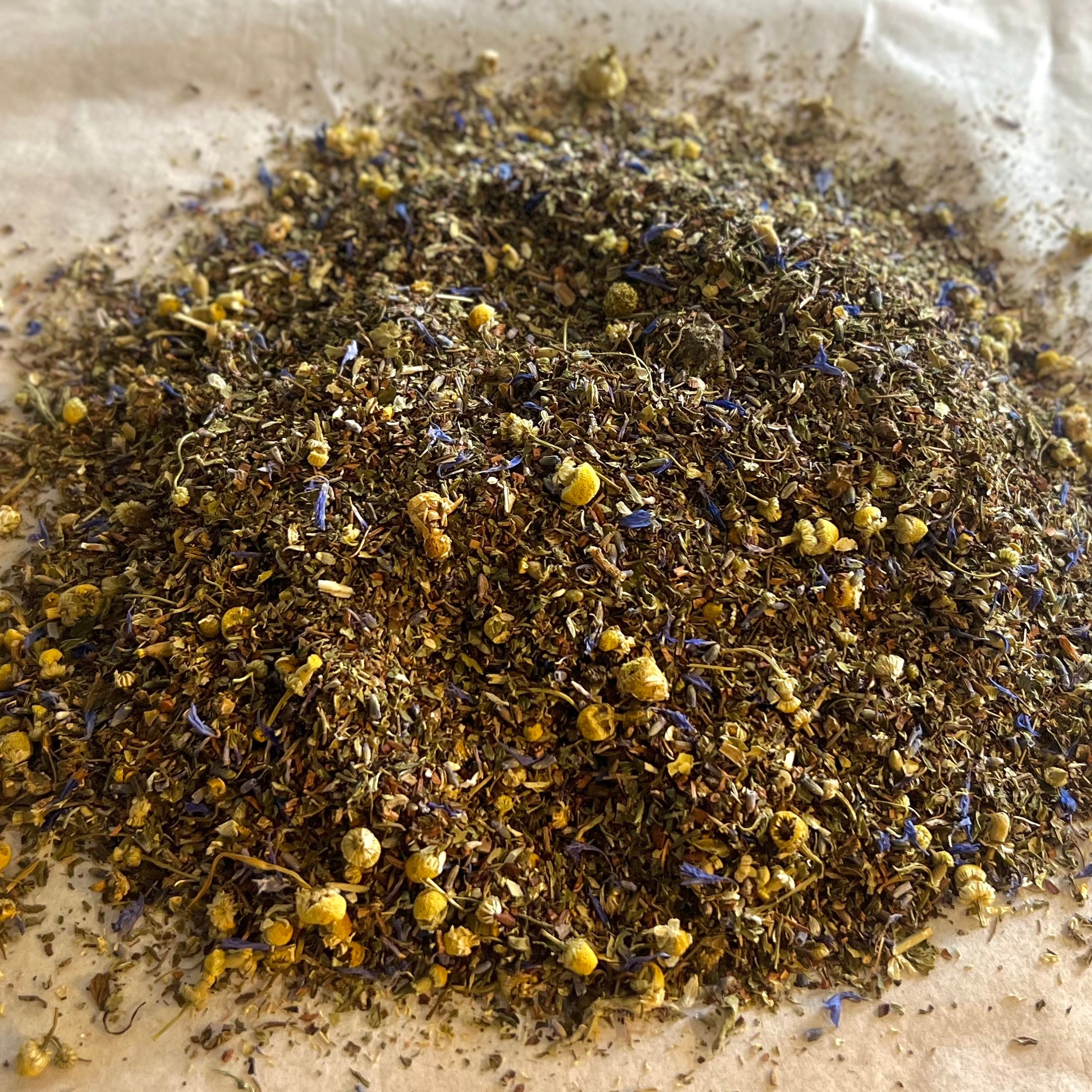 Close-up of Peaceful Sleep loose herbal tea blend with chamomile, blue cornflower petals, and calming herbs on parchment paper
