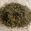Close-up of Recover Restore loose green tea blend with mixed herbs and yellow flower petals on parchment paper.