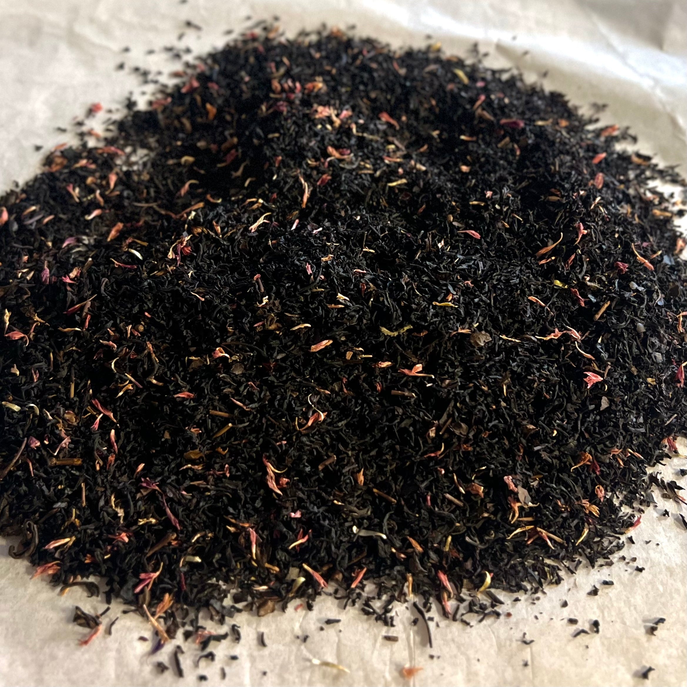 Close-up of loose Red Flower Fusion tea blend with black and oolong tea leaves and delicate red flower petals on parchment paper