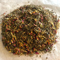 Close-up of Rose Mint Rooibos loose tea blend with rooibos leaves, rose petals, and dried mint leaves on light surface