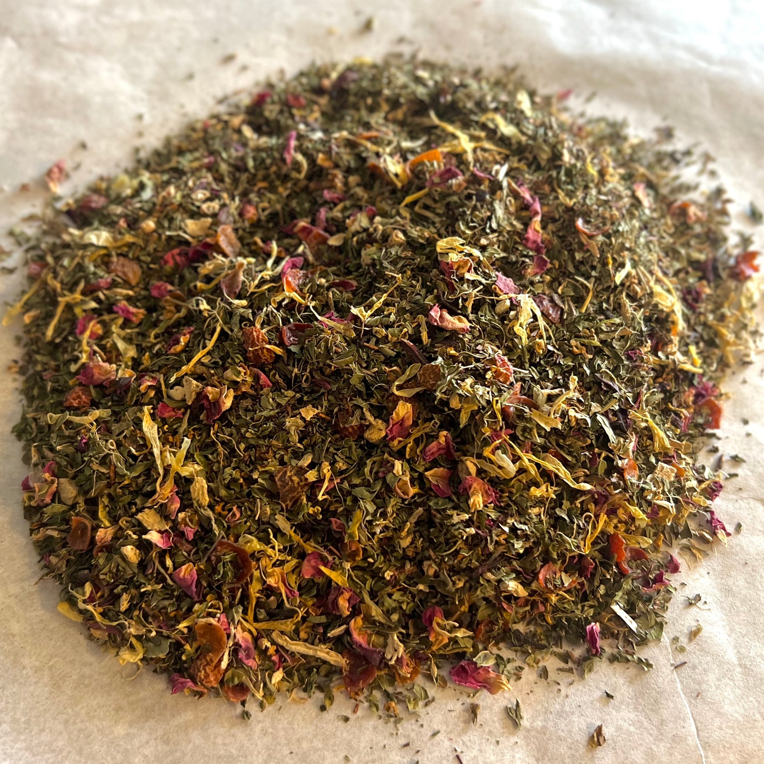 Close-up of Rose Mint Rooibos loose tea blend with rooibos leaves, rose petals, and dried mint leaves on light surface