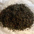 Close-up of loose Strawberry Tulsi green tea blend with dark green leaves and small red strawberry pieces on light background