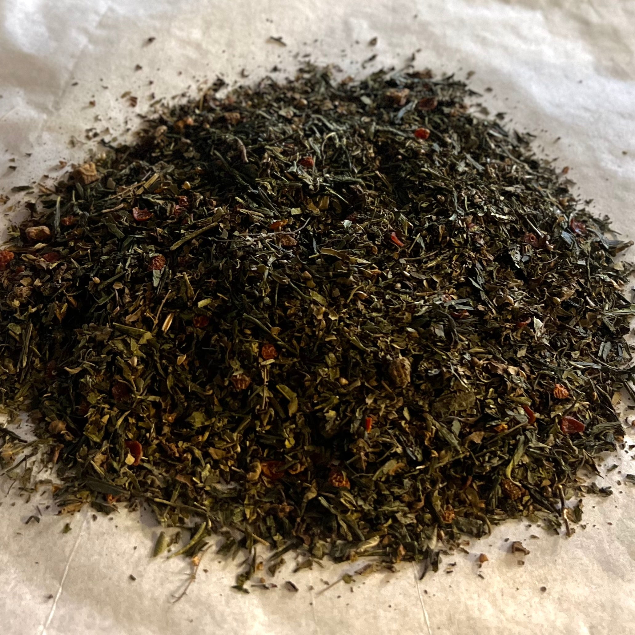 Close-up of loose Strawberry Tulsi green tea blend with dark green leaves and small red strawberry pieces on light background