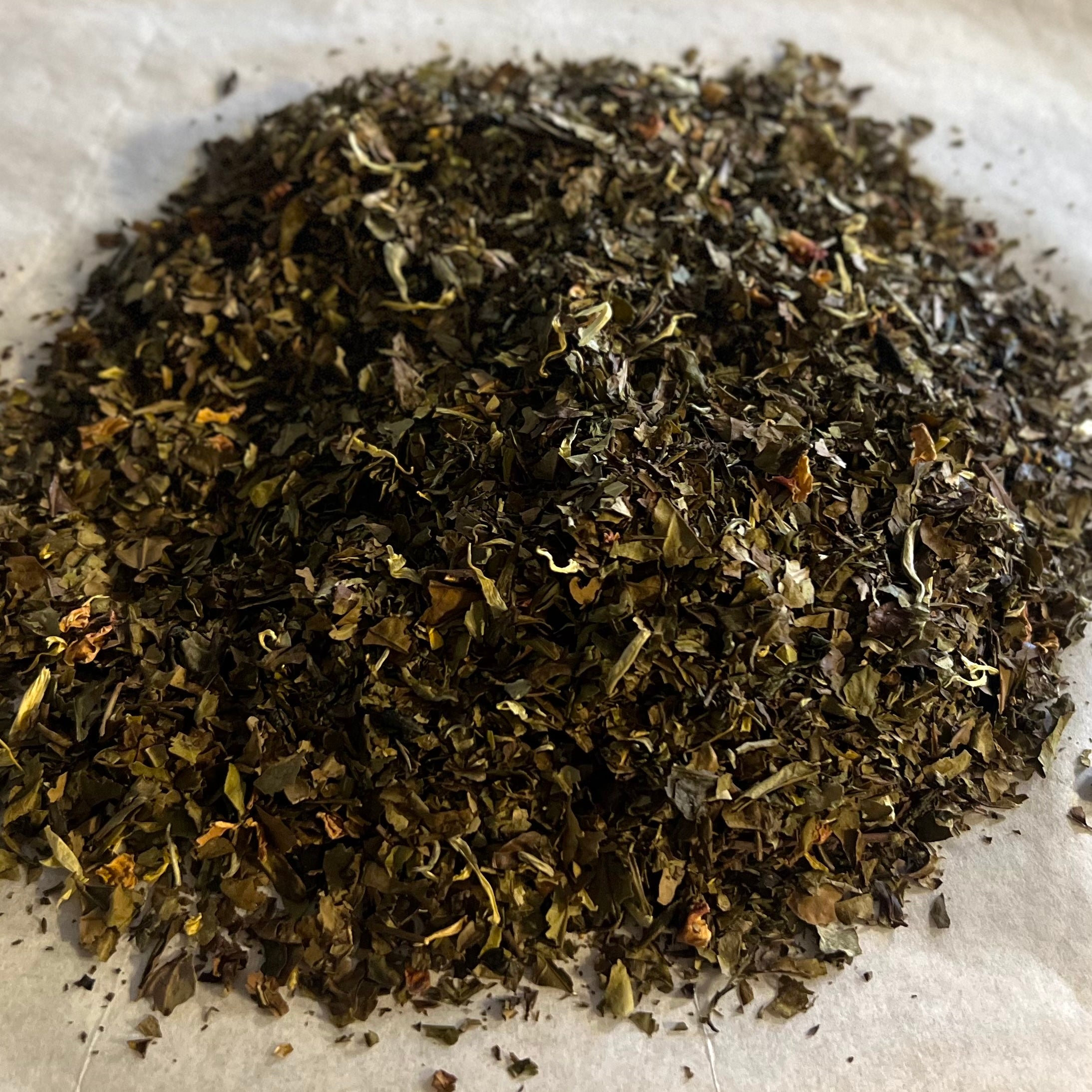 Loose Sun & Moon tea blend with mixed green and white tea leaves showing a textured, leafy dry blend on white paper.