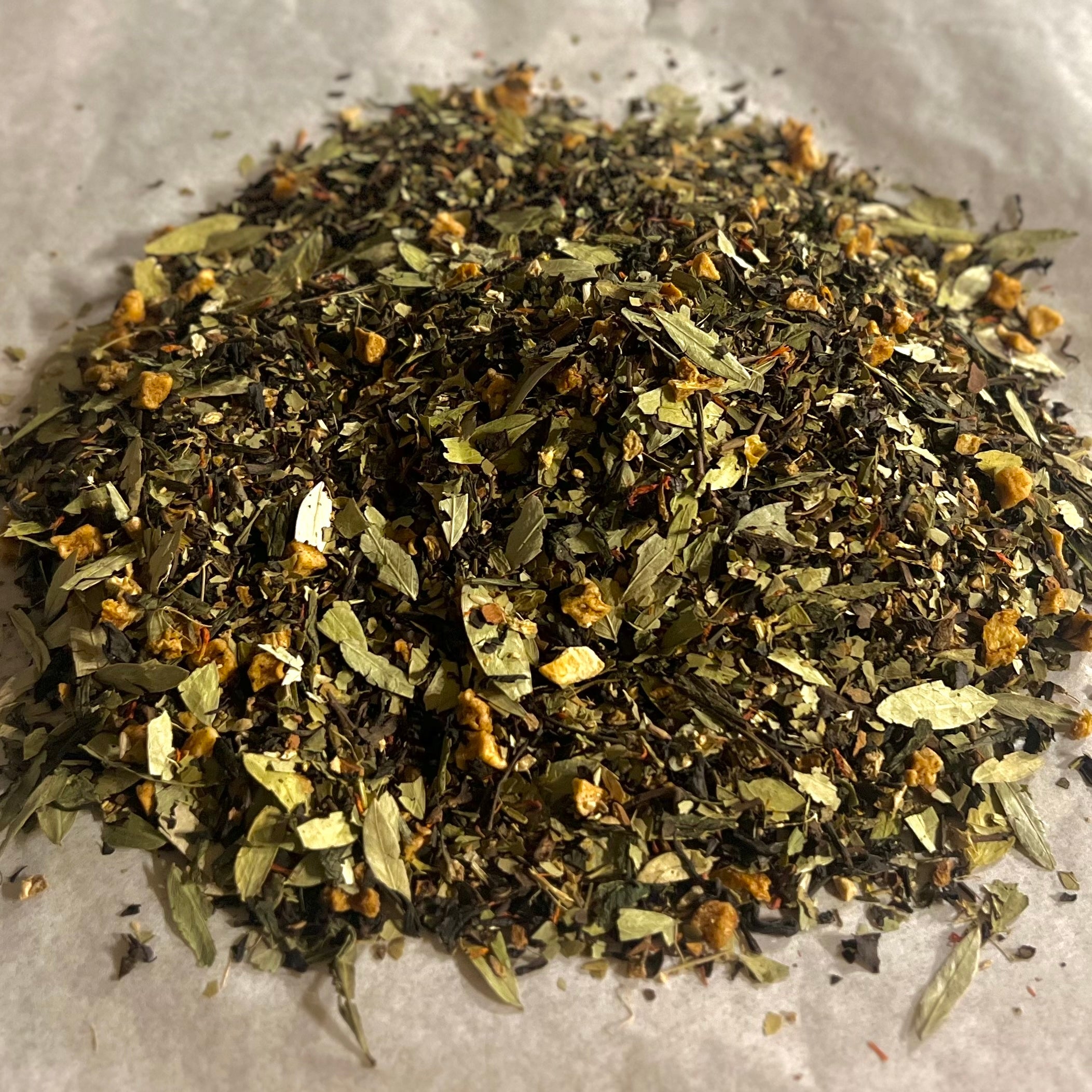 Close-up of Morning Momentum loose tea blend with green tea, mate, oolong, and herbal leaves on parchment paper surface