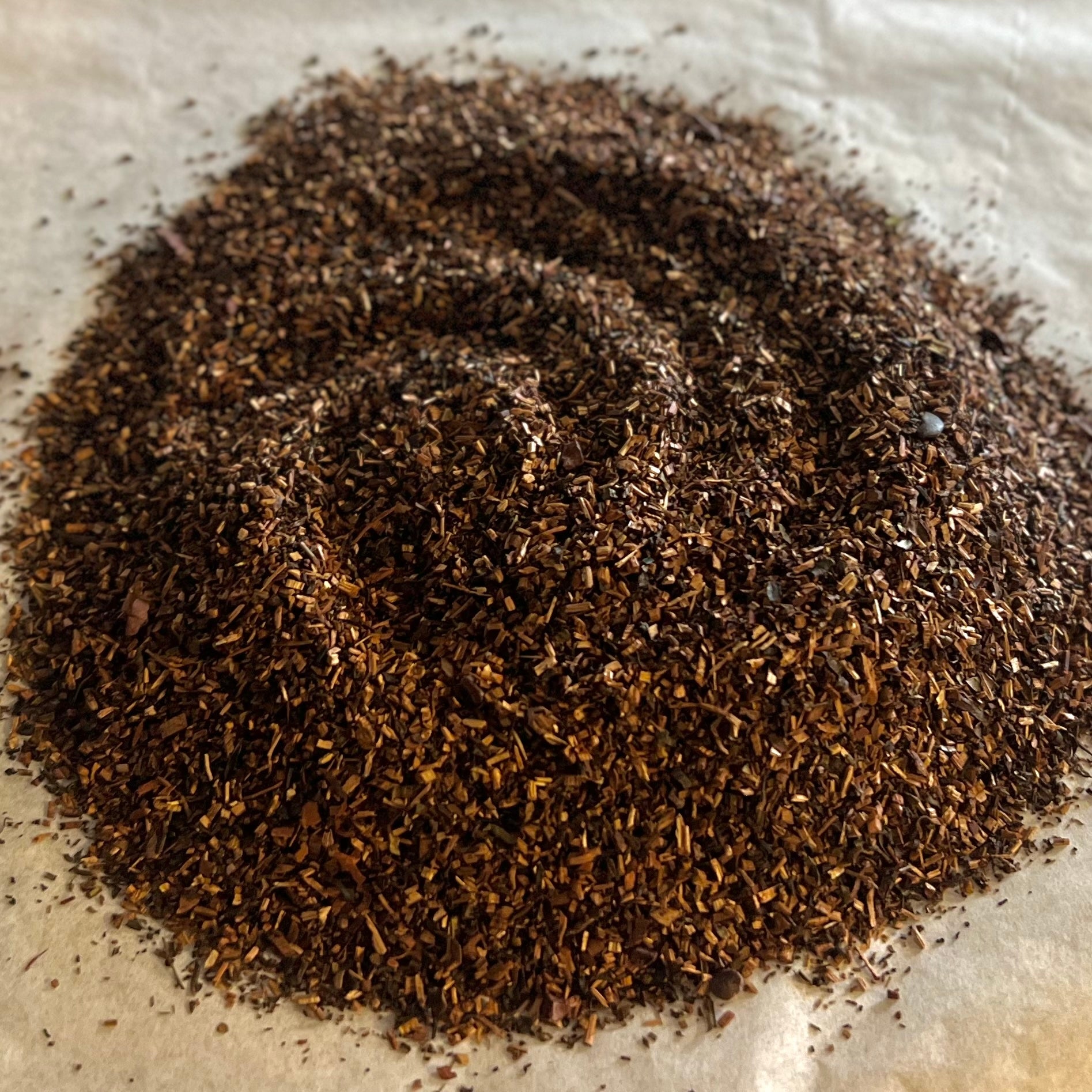 Close-up of Sweet & Subtle loose tea blend with fine cocoa nibs and dark coffee elements on parchment paper background