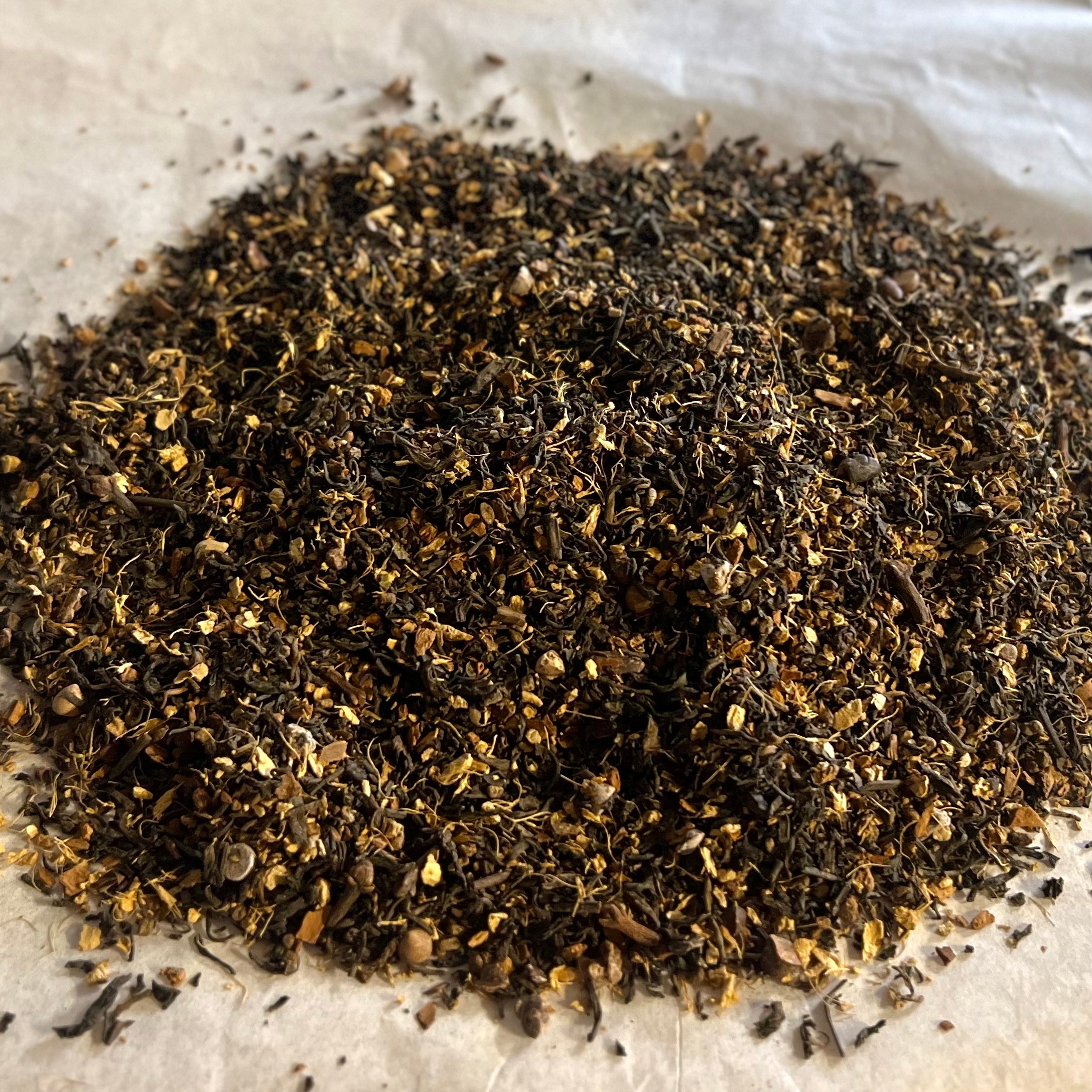 Close-up of Chai No. 32 loose tea blend with dark pu-erh leaves, cocoa nibs, and chai spices on a parchment surface