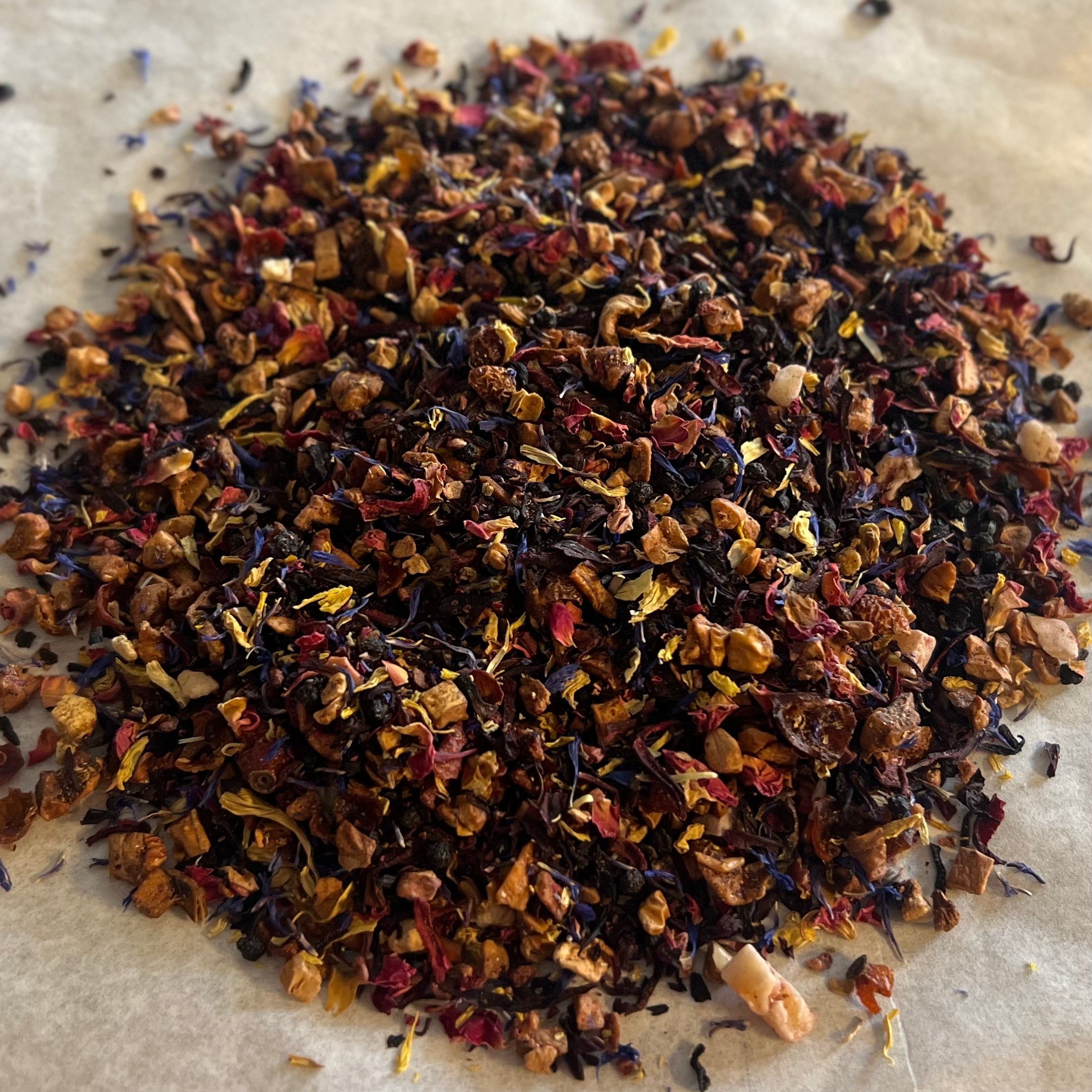 Close-up of Through the Valley loose fruit and herbal tea blend with vibrant dried petals and fruit pieces on parchment paper
