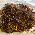 Close-up of loose Triple Berry tea blend with honeybush, dried berries, and fruit pieces on a light surface.