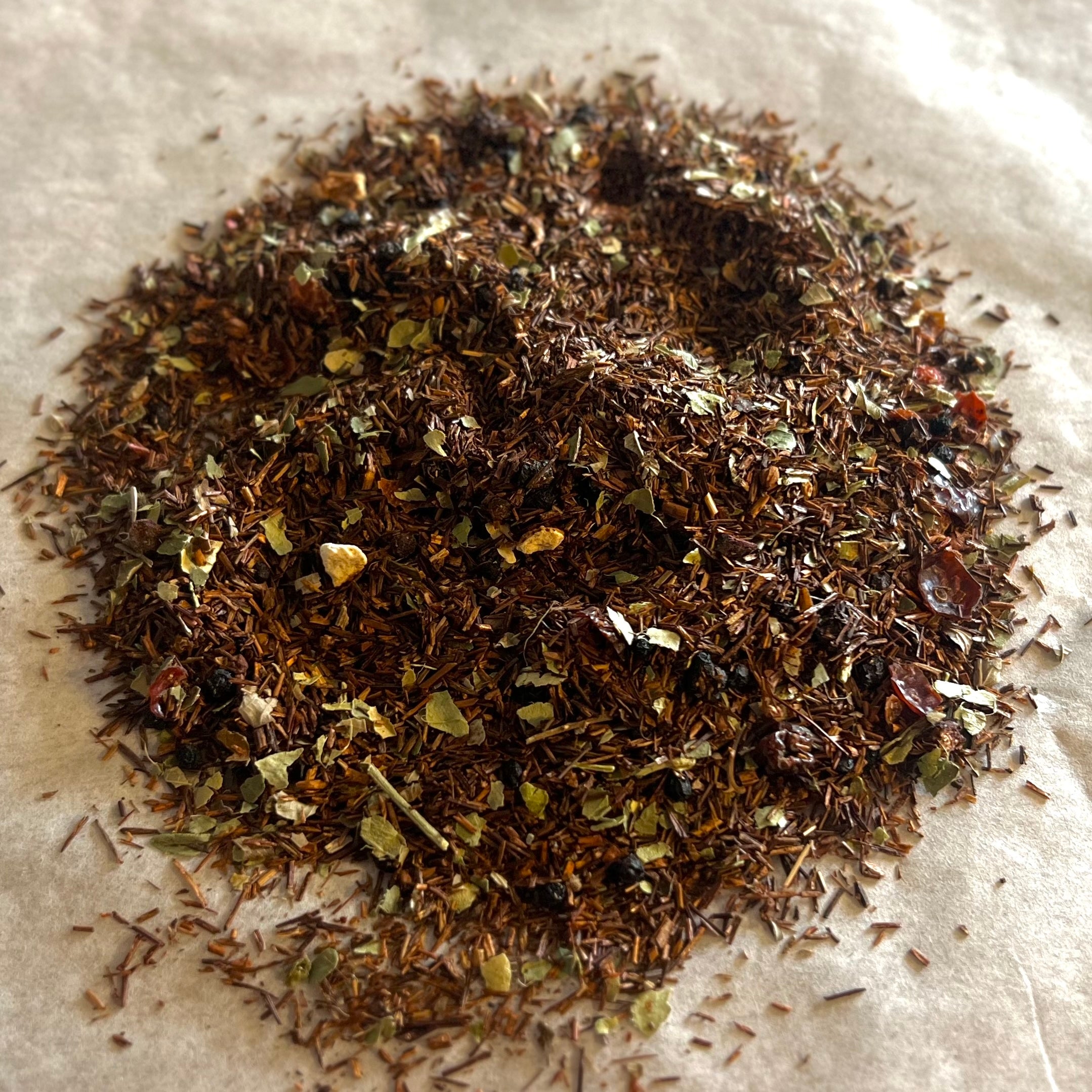 Close-up of Trust the Elders loose rooibos tea blend with mixed herbs and natural immunity-boosting ingredients on parchment paper.