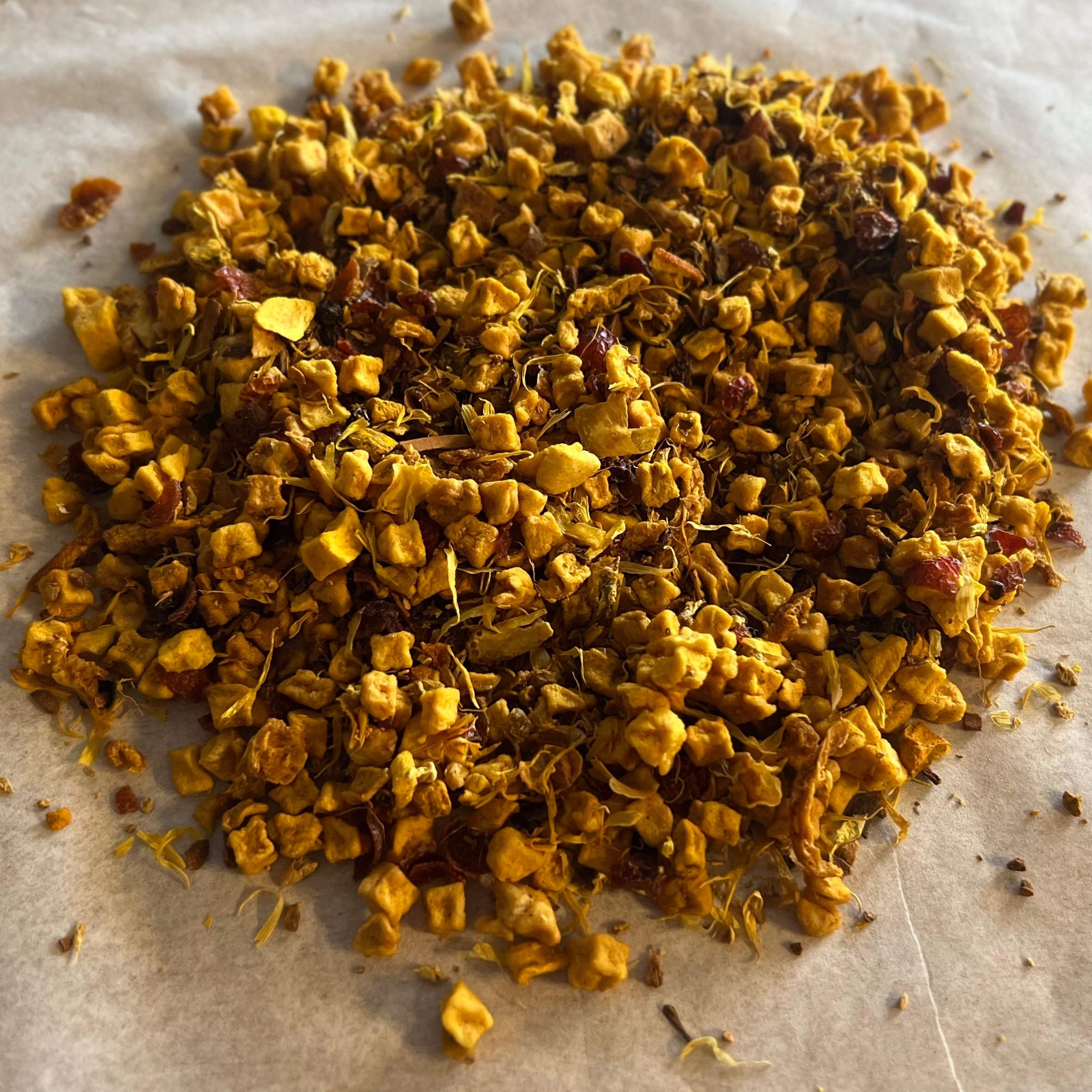 Close-up of Turmeric Fusion loose tea blend with turmeric pieces, dried mango bits, and orange zest on parchment paper.