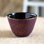 Close-up of purple cast iron drinkware with honeycomb texture and glossy black interior on woven mat surface