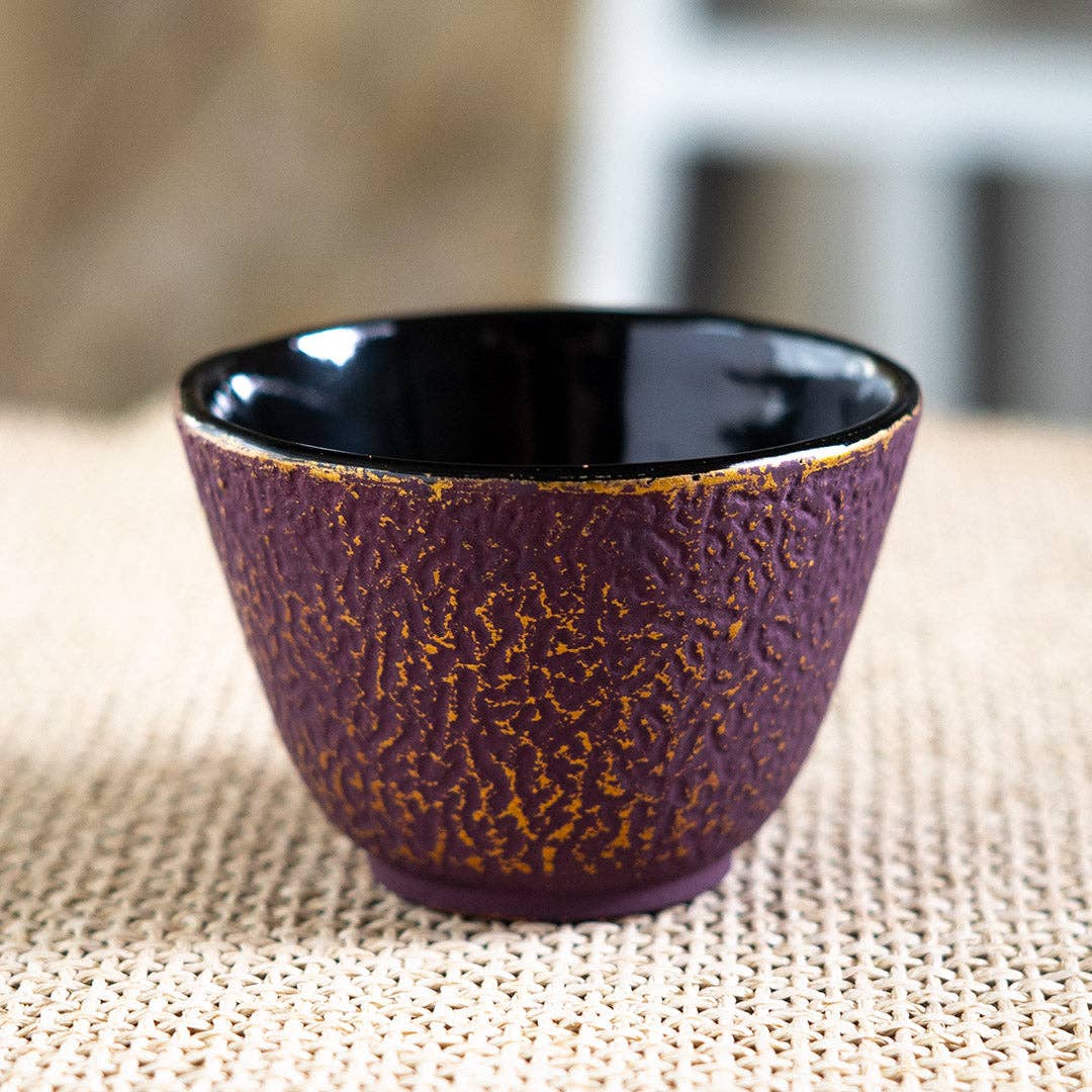 Close-up of purple cast iron drinkware with honeycomb texture and glossy black interior on woven mat surface