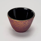 Close-up of purple honeycomb textured cast iron cup with smooth black interior on plain light background