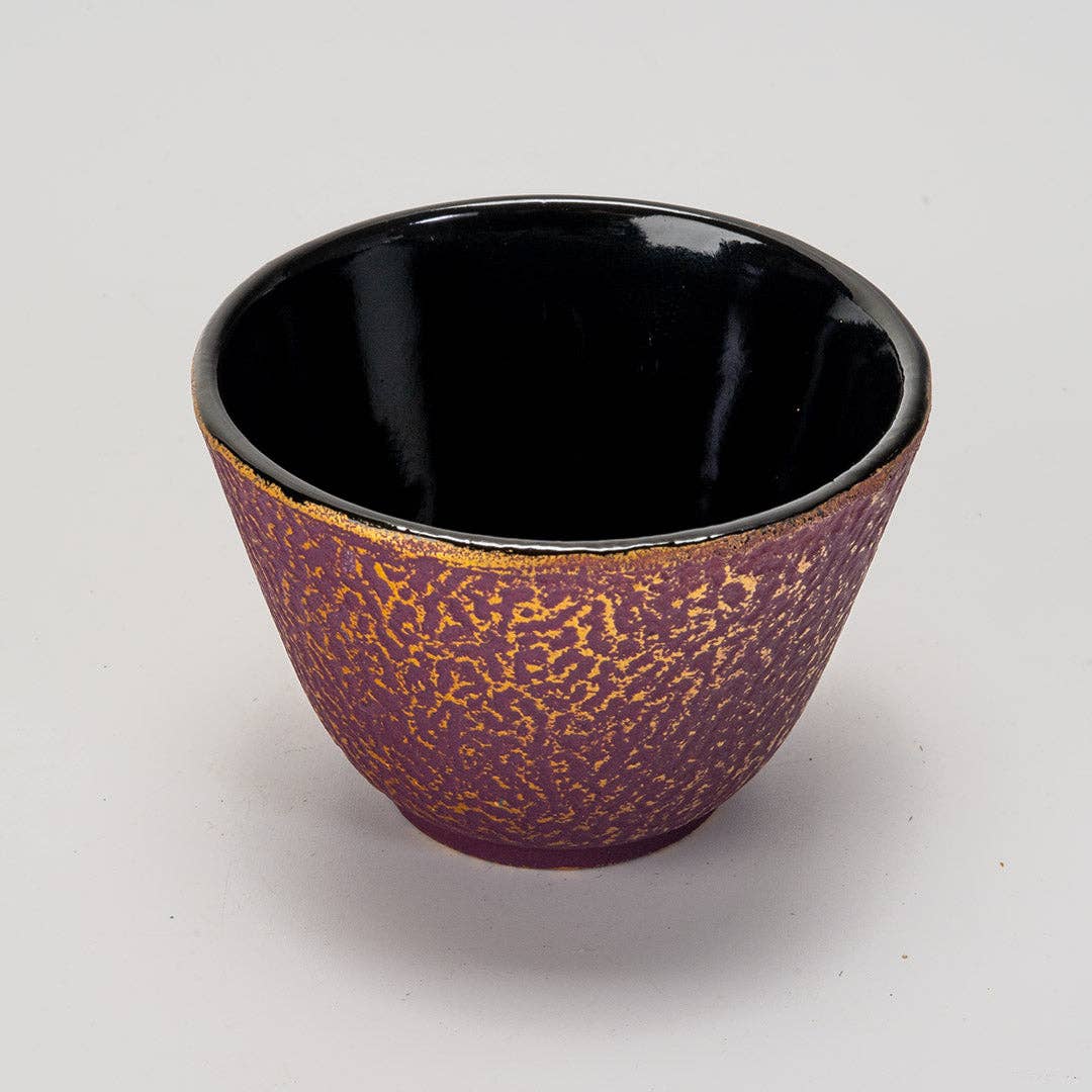 Close-up of purple honeycomb textured cast iron cup with smooth black interior on plain light background
