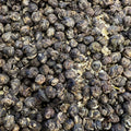 Close-up of Jasmine Phoenix Pearl tea showing tightly rolled green tea leaves with jasmine blossoms and light petals.