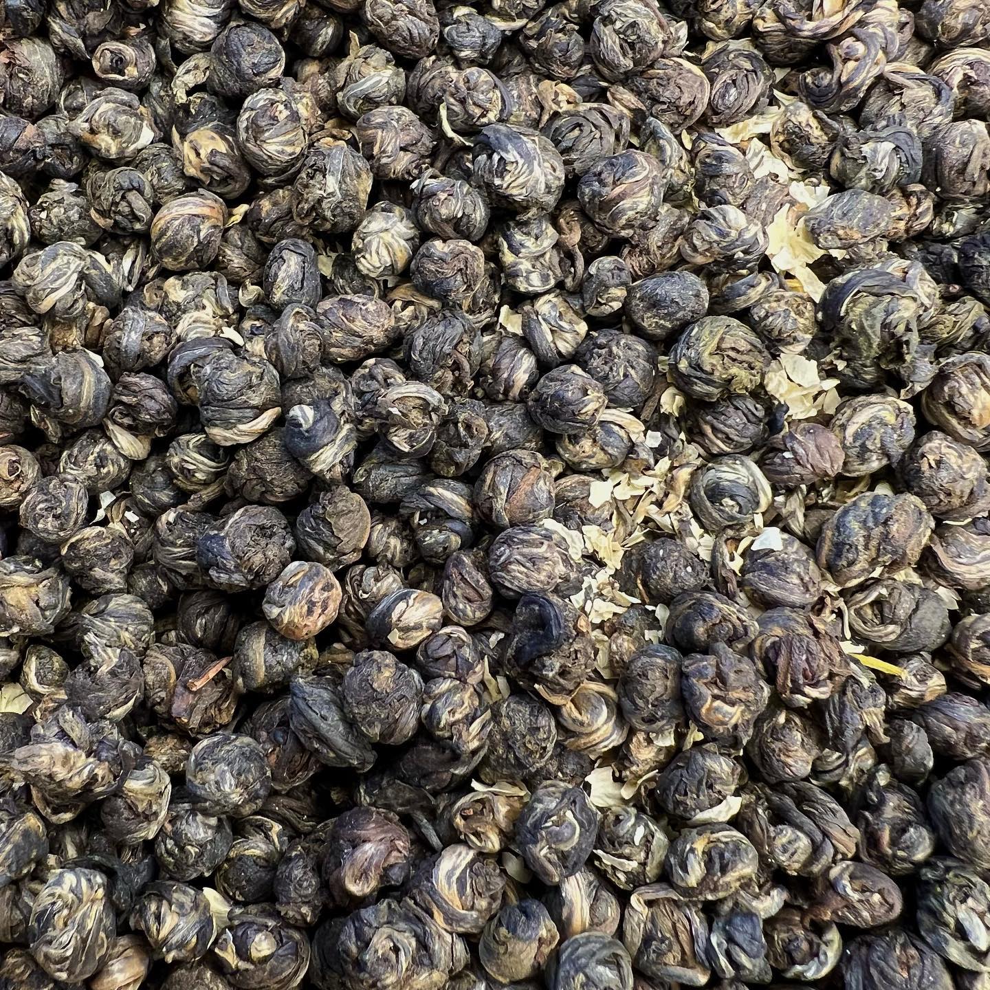 Close-up of Jasmine Phoenix Pearl tea showing tightly rolled green tea leaves with jasmine blossoms and light petals.