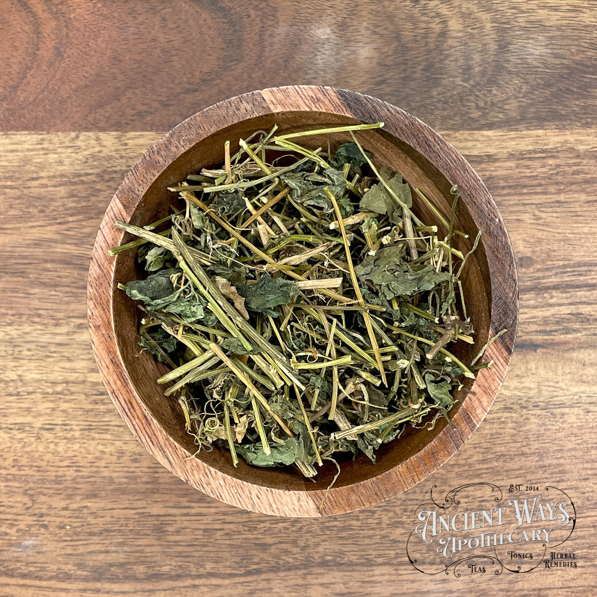 Wooden bowl filled with dried herbs on a wooden surface, branded 'Ancient Ways Apothecary'.