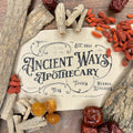Close-up of dried Chinese herbs including Du Zhong, Niu Xi, Gou Qi Zi, and red dates arranged around apothecary label on wood surface