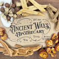 Dried Chinese herbs including roots, nuts, and fruit pieces arranged around an Ancient Ways Apothecary label on wood.