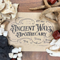 Vintage-style Ancient Ways Apothecary label surrounded by dried Chinese herbs including Dang Gui and Hong Zao on wood surface